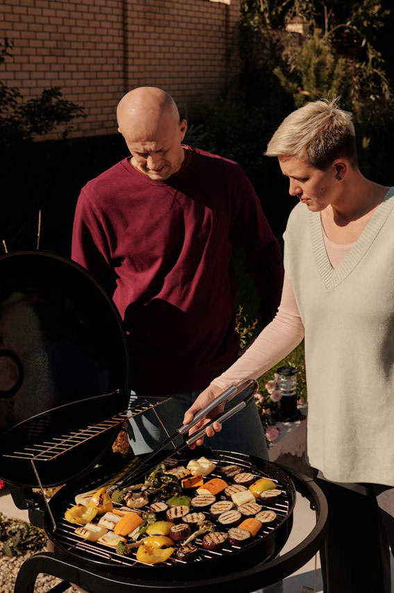 Ein Grill steht im Garten und zwei Personen wenden Grillfleisch.